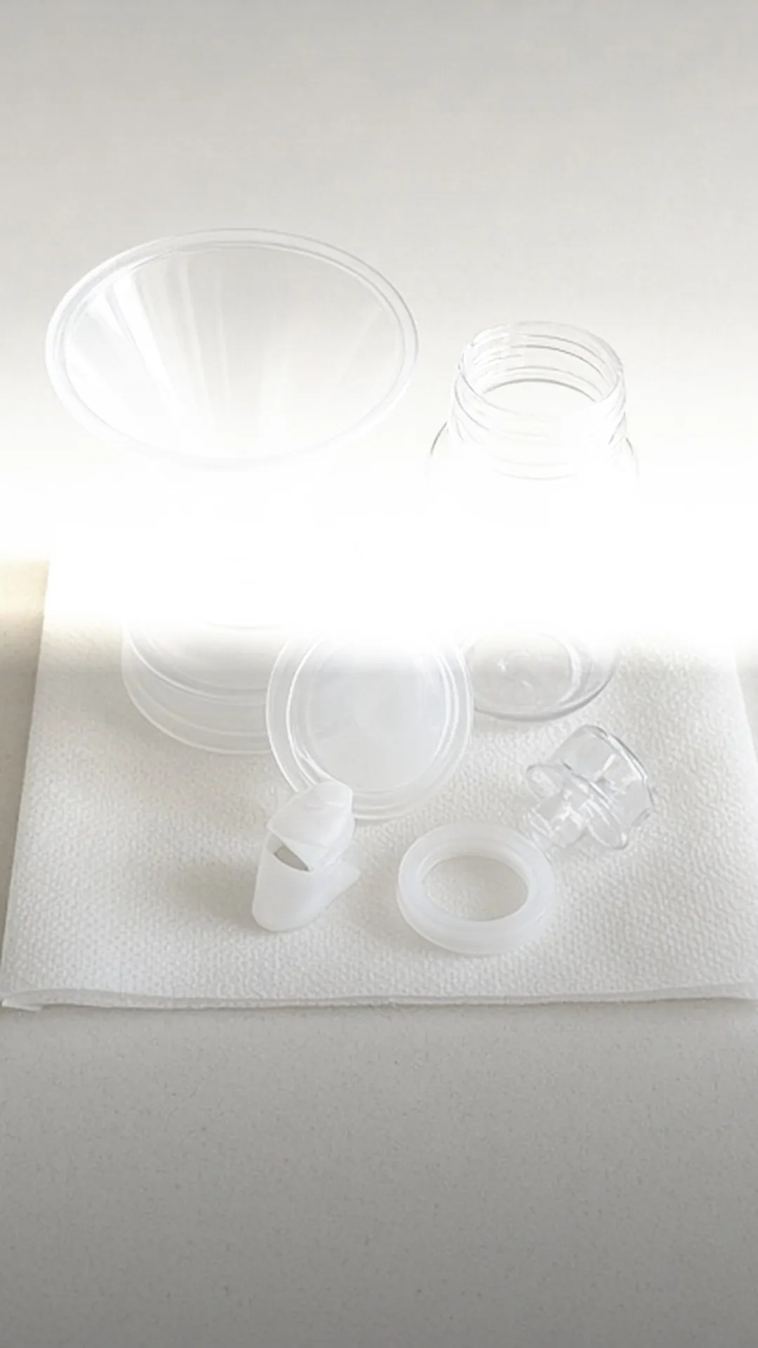 A breast shield, a bottle, and four small pump parts on a white paper towel