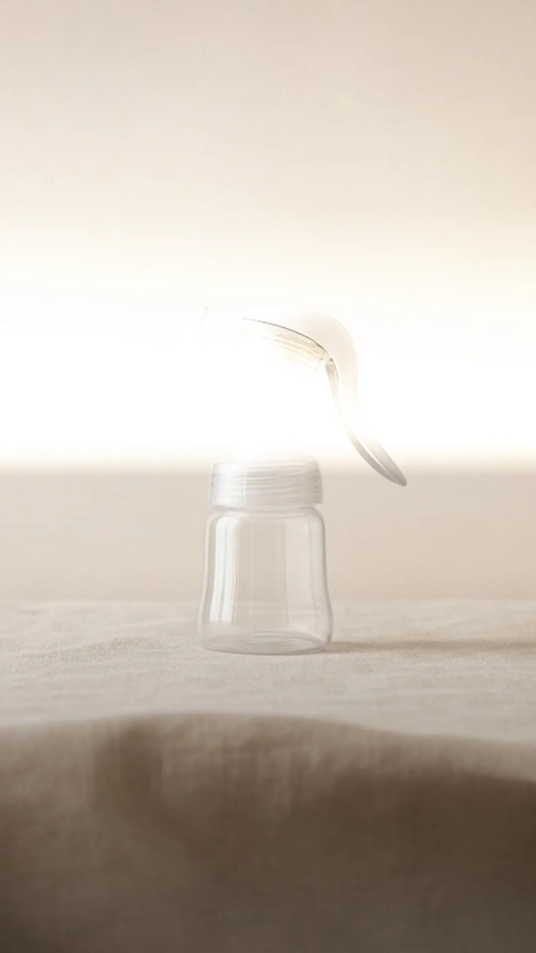 One clear manual breast pump with a white lever handle on pale linen