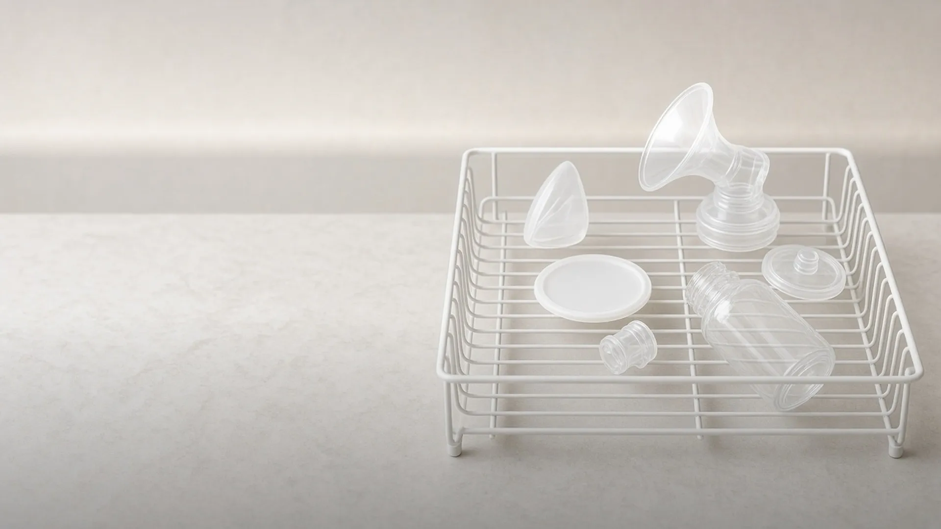 A breast shield, a bottle, and four parts in a white wire rack on stone